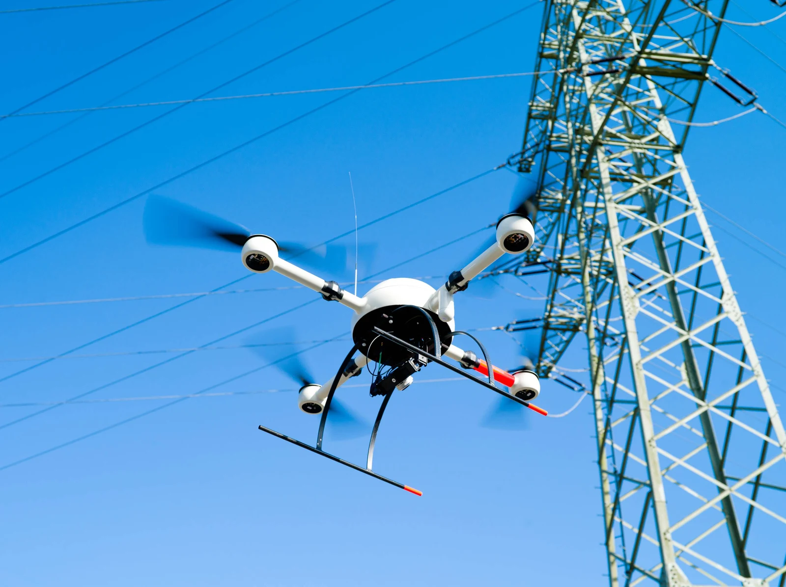 Multi-rotor drone conducting close-range inspection beside a transmission tower.